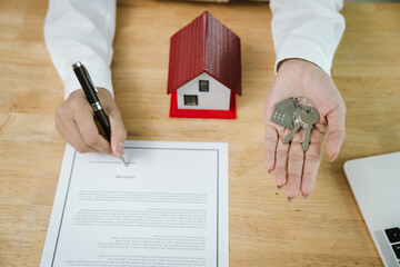 A real estate agent signs a sales contract with a house model and keys on the table, symbolizing...