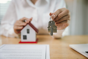 A real estate agent signs a sales contract with a house model and keys on the table, symbolizing...