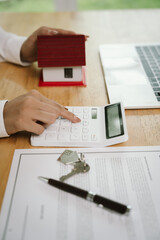 A real estate agent signs a sales contract with a house model and keys on the table, symbolizing...