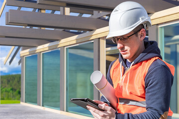 Construction. Architect or engineer in hard hat and safety vest holding blueprints and tablet at modern building site, architecture, design, project management.