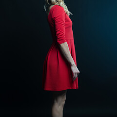 Elegant blonde woman posing in red dress on black background