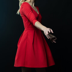 Elegant blonde woman posing in red dress on black background