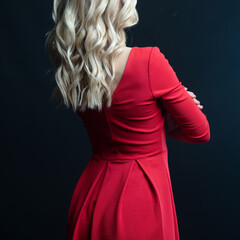 Elegant blonde woman posing in red dress on black background