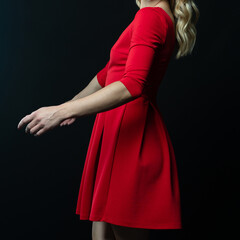 Elegant blonde woman posing in red dress on black background