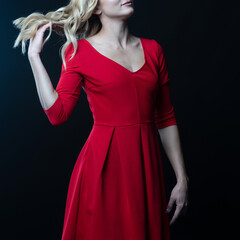 Elegant blonde woman posing in red dress on black background
