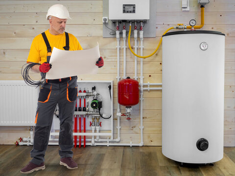 Heating installation, plumber engineer checking blueprints near boiler system, hot water tank, central heating, household utilities maintenance