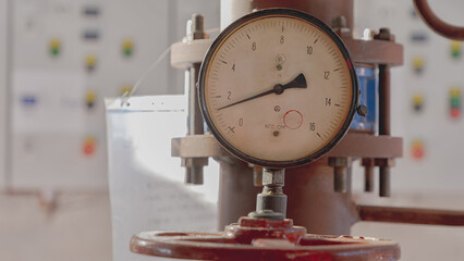 Old pressure gauge in a boiler room with control panels in the background