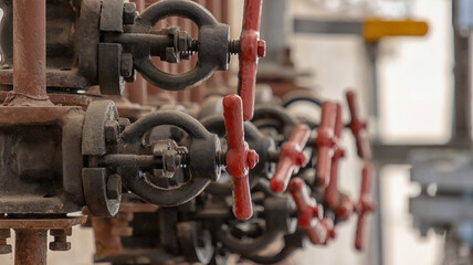 Valves and piping in a boiler room, with red valves on a blurred background of equipment