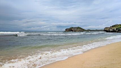 Tranquil Sundak Beach Scene with Waves, Sand, and Distant Rock Formation in Gunungkidul, Yogyakarta, Indonesia