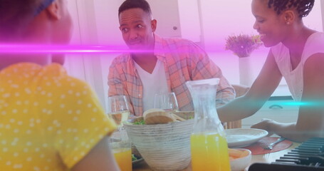 Parents and daughter sharing breakfast in home kitchen, with bread rolls and orange juice