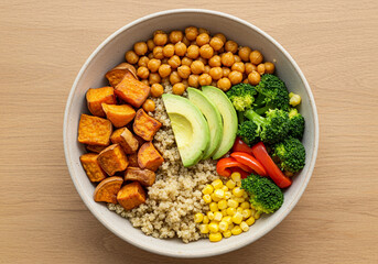 Quinoa and Veggie Buddha Bowl: A top-down view of a colorful, healthy Buddha bowl filled with quinoa, sweet potatoes, chickpeas, avocado, broccoli, and corn on a light wooden background