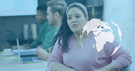 Sitting Hispanic woman in pink sweater listening at conference table, laptops, globe overlay