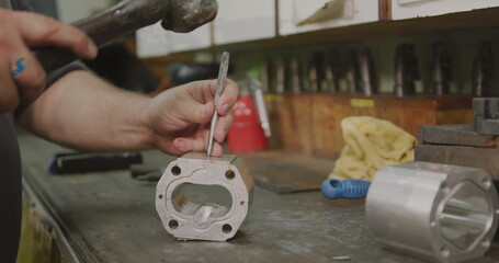 Striking machined aluminum block on metal workshop bench by worker's hands, with hammer and chisel