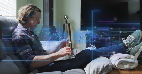 Man in plaid shirt typing on laptop, holding credit card in living room, with circuitry overlay
