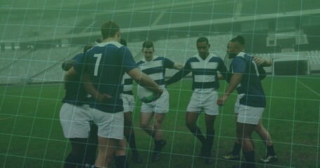 Huddling seven athletes wearing striped jerseys on grass pitch in empty stadium, with rugby ball
