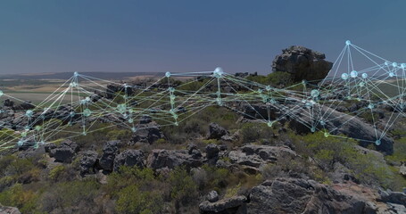 Overlaying glowing network spanning rocky hillside under clear blue sky, overlooking farmland