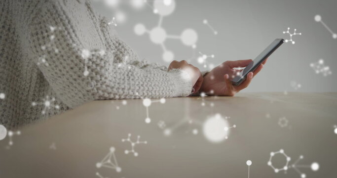 Holding smartphone, sweater-clad woman interacting on wooden table, molecular overlay, copy space - Powered by Adobe
