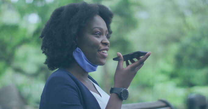 Executive in navy blazer, mask speaking into smartphone and checking smartwatch in park, copy space - Powered by Adobe