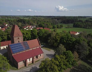 Aerial view of a red-roofed church with solar panels, nestled in a verdant rural landscape