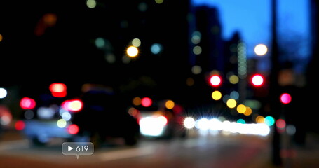Moving blurred cars and bokeh lights illuminating downtown street at dusk, showing traffic lights