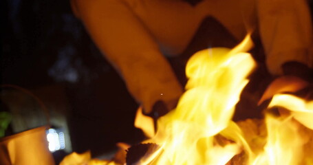 Fototapeta premium Crackling flames roaring around logs in outdoor fire pit, with boots and pants above