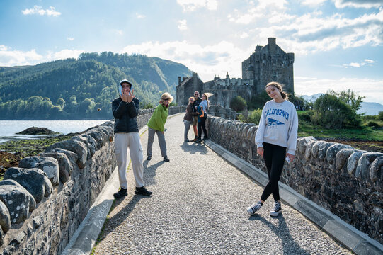 Family of tourists walking on stone bridge towards Eilean Donan Castle in Scotland on a sunny day