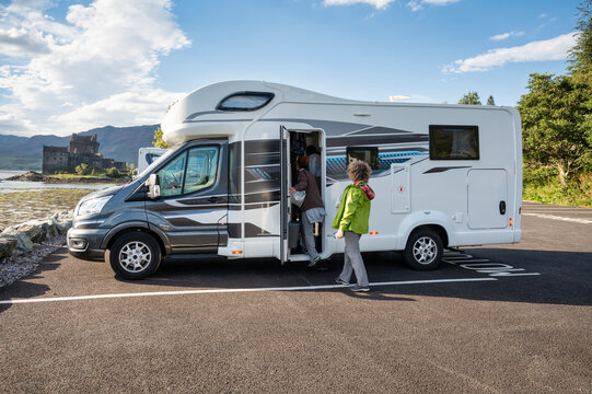 Two adult sisters boarding their motorhome after exploring the stunning Eilean Donan Castle in the Scottish Highlands, parked beside a scenic loch under a blue sky
