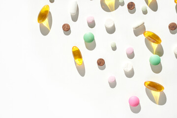 Colorful assortment of various pills and capsules on white background with shadows.
