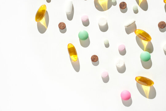 Colorful assortment of various pills and capsules on white background with shadows.