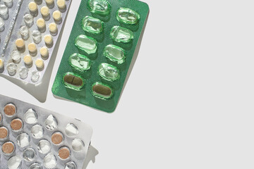 Assorted blister packs of green and yellow pills on light gray background with shadows.