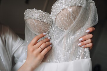 Young bride holding lace white dress in her hands in the morning in hotel room. Wedding photography.