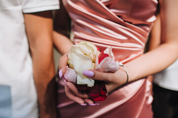 Photograph of many colorful rose petals in hands of female guest at wedding ceremony.