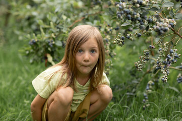 The girl squats down and looks in front of her in surprise. The child has blond hair and blue eyes.