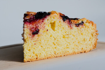 Close-up of plum cake slice with golden crust and juicy baked plums on wooden board. Homemade rustic dessert, sweet and fresh.
