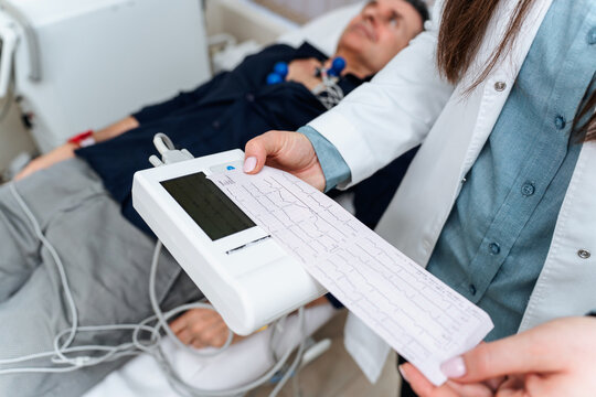 Female doctor examining electrocardiogram paper result in hospital, performing medical activity using portable medical device for electrocardiogram test