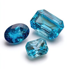 Three vibrant, light-blue gemstones, showcasing different cuts, sit on a plain white surface