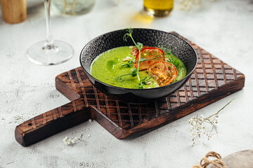 Bowl of green vegetable soup topped with tomato chips and greens