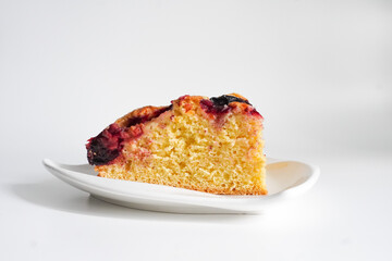 Close-up of plum cake slice with juicy baked plums and golden crust on white plate. Rustic homemade dessert in minimalist style.