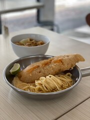 Delicious crispy fish fillet and pasta in a bowl and pan