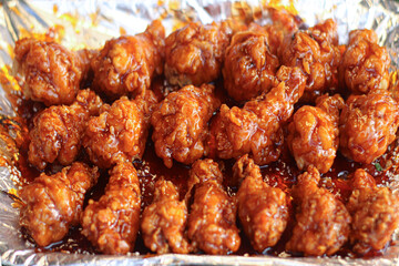 Thai spicy caramel fried chicken wing drumettes on foil tray. Golden brown crispy texture glazed with sweet and spicy sauce, authentic Asian street food style.