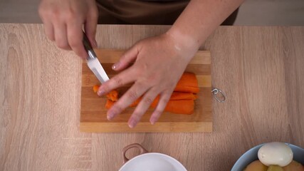 Female hand using a sharp knife cutting boiled carrot on wooden cutting board. Preparing ingredients for boiled vegetables salad - Powered by Adobe