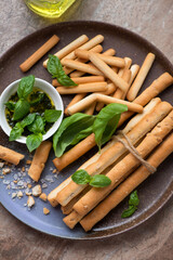 Various breadsticks with basil oil and fresh basil served on a brown plate, middle close-up, vertical shot, elevated view