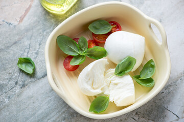 Beige serving tray with buffalo mozzarella and green basil, horizontal shot on a grey granite background, high angle view