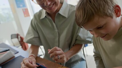 Tilt up of young female teacher and clever schoolboy connecting colorful wires to circuit board on desk while carrying out technical assignment at lesson