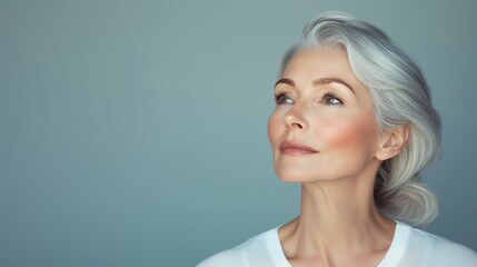 Fototapeta premium Elegant mature woman with silver hair looking up thoughtfully. Beauty and confidence portrait with minimal background. Aging gracefully concept.