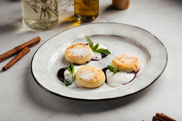 Delicious cottage cheese pancakes served with sour cream, fresh mint, and berry sauce on a white plate