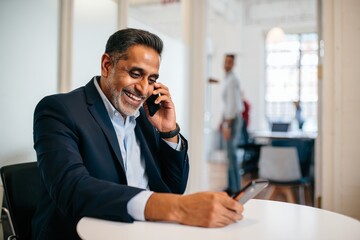 Smiling Businessman Talking on Phone and Writing on Tablet