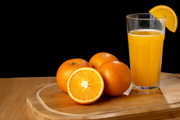 Orange juice in a glass and oranges on a wooden surface on a black background
