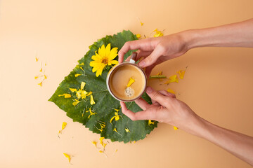Cup of coffee decorated with a yellow flower petal on a large green leaf, surrounded by scattered...