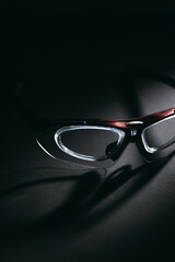 Red and black sports safety glasses on dark surface with dramatic shadows